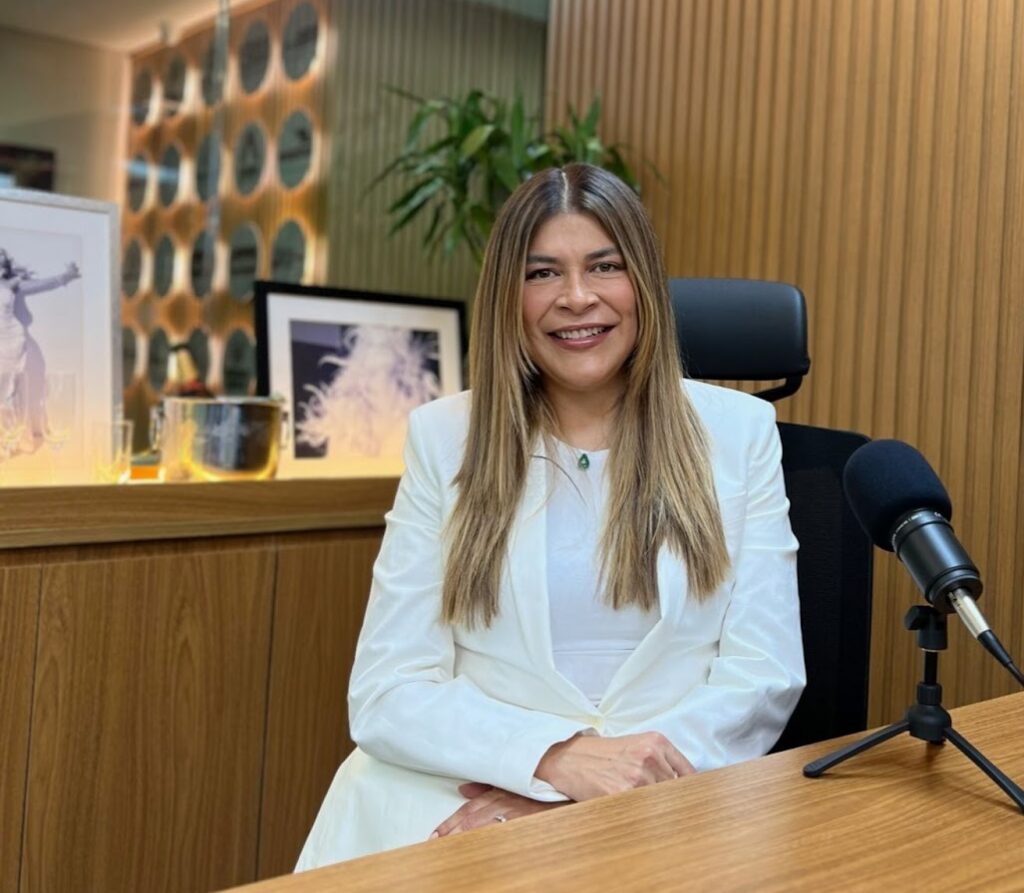 Lu Rodrigues sorrindo sentada em um cenário de podcast